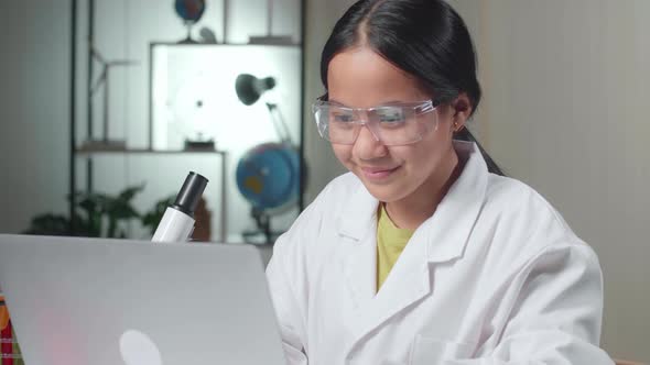 Asian Scientist Girl Looking At Microscope  And Work With Laptop Computer. Child Learn With Interest