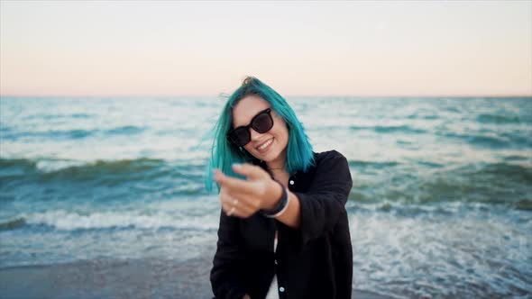 Unusual Woman with Blue Dyed Hair Dancing, Spinning Hands Around on Sea Background. Femininity