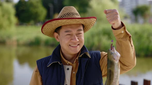 Close View of the Asian Man Wearing Special Fishing Clothes Holding the Fish He Caught on the Hook