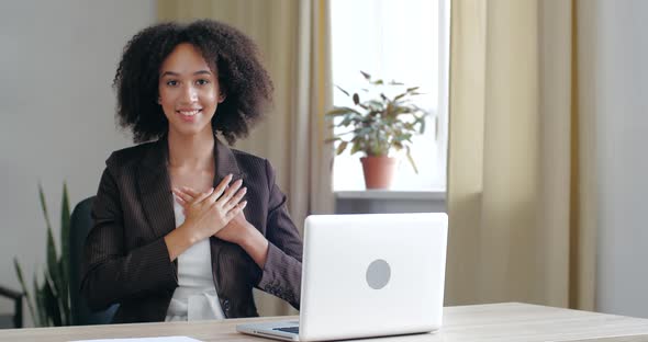 Curly Smiled Millennial Business Woman Sitting at Office Home Table, Put Folded Palms on Heart