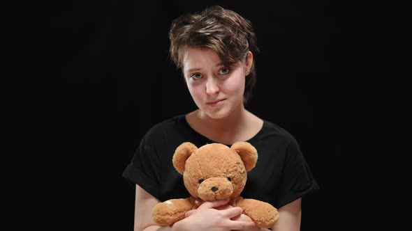 Young Brunette Woman with Sad Smile Holding Teddy Bear Looking at Camera