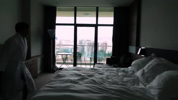 Happy Young Man Jumping on Bed at Hotel in Bathrobe