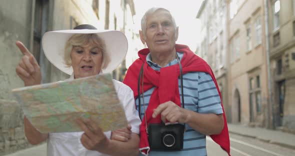 Senior Male and Female Tourists Walking with a Map in Hands Looking for Route