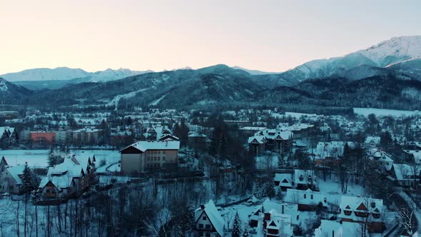 Aerial Footage Of SnowCapped Mountains In A Town With Snow Covered Houses And Trees