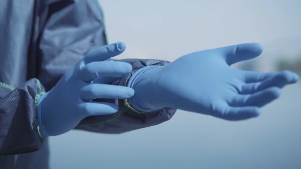 Close-up of Human Hand Putting on Blue Protective Glove. Unrecognizable Worker in Antiviral Suit