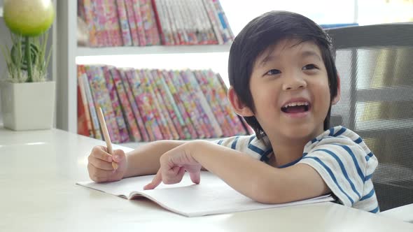 Little Asian Child  Using A Pencil To Write On Notebook At The Desk