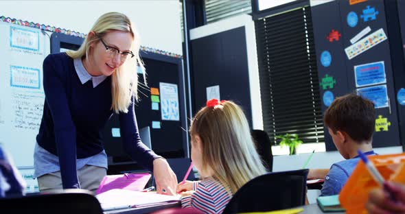 Teacher helping schoolgirl with her homework in classroom