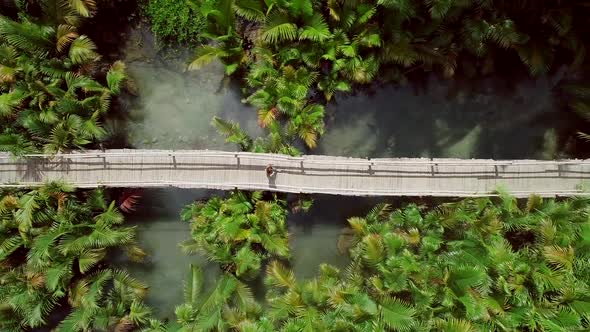 Aerial view of woman walking on long wooden bridge in Bojo river, Philippines.