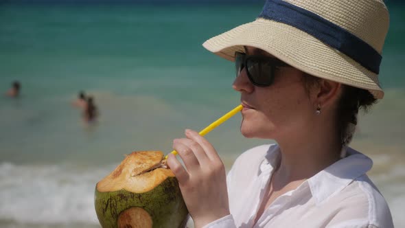 Woman in Hat Drinks Coconut on the Beach