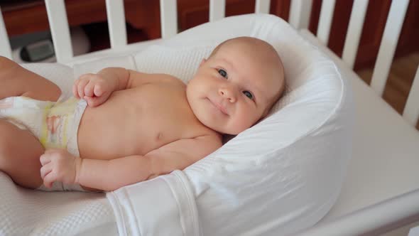 Cute Little Newborn Baby Lies in a Crib in a Newborn Cocoon and Shows Tongue Funny