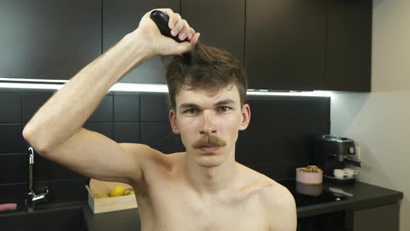 Man with mustache shaves his head with electric trimmer at home during quarantine