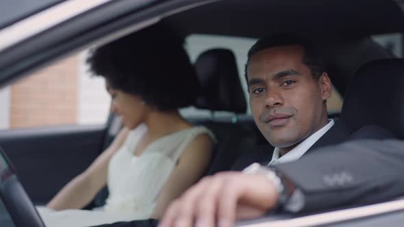 Portrait of Happy Confident Groom Sitting on Driver's Seat Looking at Camera Smiling with Bride at