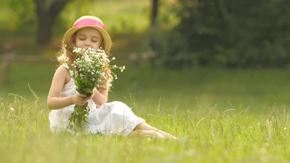 Child Holds a Bouquet of Wildflowers in Her Hands, She Smells Them and Smiles