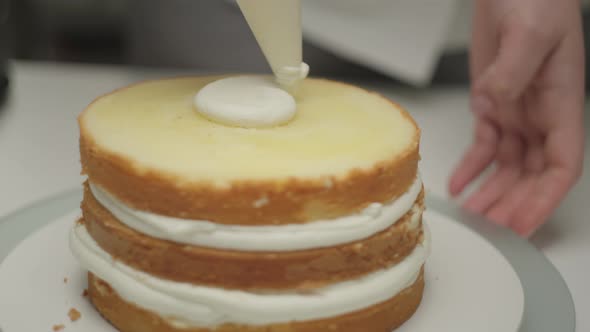 Chef's Hands Squeezing Cream on Rotating Biscuit Cake Layers Using Confectionery Bag