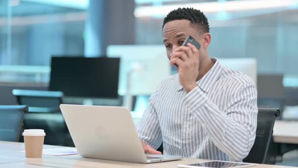 African Businessman with Laptop Talking on Smartphone