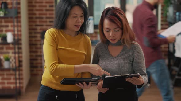 Asian Women Comparing Statistics on Clipboard and Tablet