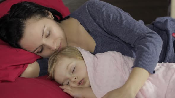 Young Mother Sleeping with Her Little Baby Daughter. Family Sleeping on the Bed