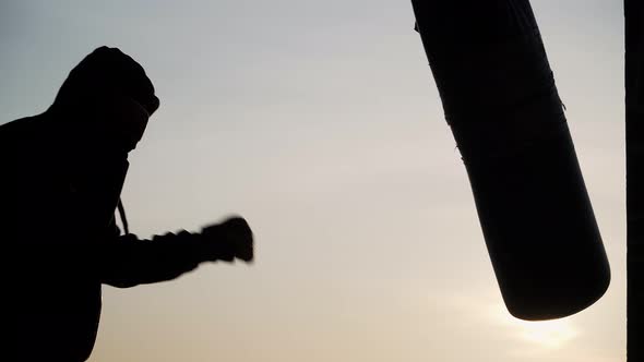 Boxer beats punching bag on sunset background. Silhouette motivation sport boxing.