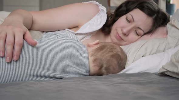 Mother in Breastfeeding Newborn Relaxing on Bed