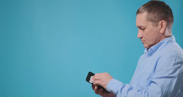 Aged Man in Blue Shirt Disinfects Smartphone with Napkin