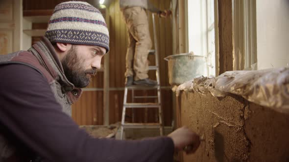 An Asian man plastering his house walls with a clay render