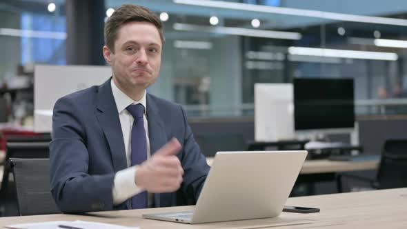 Businessman Showing Thumbs Up Sign While Using Laptop in Office