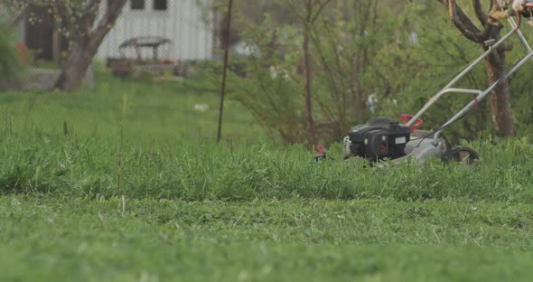 Green Grass in the Garden and Man with a Lawn Mower in Slow Motion is Passing By