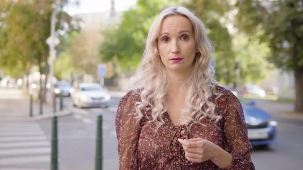 A Middleaged Caucasian Woman Shakes Her Head at the Camera with a Frown in an Urban Area