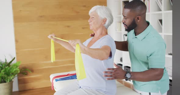 Video of happy caucasian senior woman exercising with african american male physiotherapist
