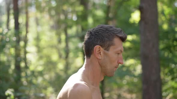 Side View Tracking Shot of Confident Topless Sportsman Walking in Sunbeam in Summer Forest Looking