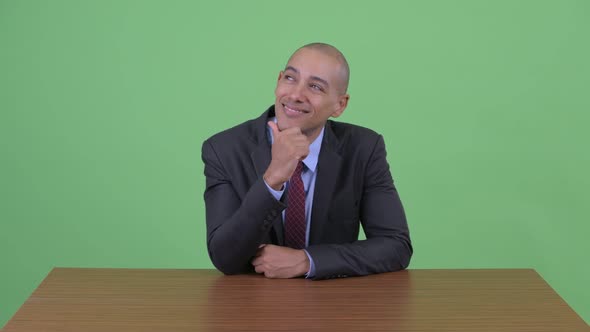 Happy Bald Multi Ethnic Businessman Thinking Behind Desk