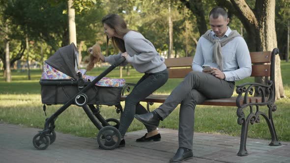 Wide Shot of Joyful Caucasian Mother Playing Teddy Bear with Infant in Baby Stroller As Concentrated