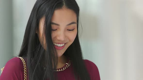 Close up of Asian woman looking at her phone and smiling then looking around then looking back at he