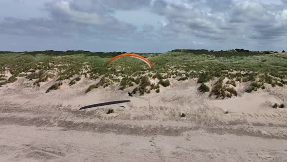 Paraglider playing swinging back and forth close to Dutch waterfront sand dunes