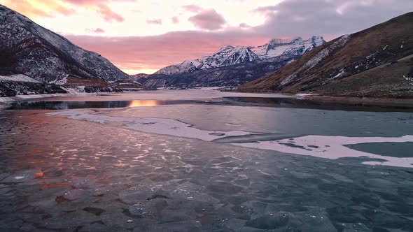 Flying over winter landscape toward snow capped mountain at sunset