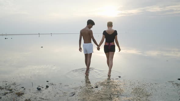 Back View of Interracial Couple Walking in Shallow Sea Water at Sunset Slow Motion Entering Water