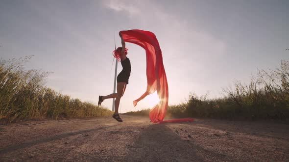 Woman with Pieces of Red Cloth Dance Near the Field with Wind Generators 