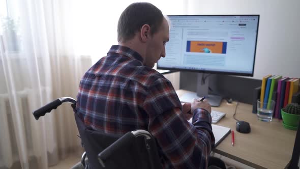 A Disabled Worker Sitting in a Wheelchair Works at a Computer