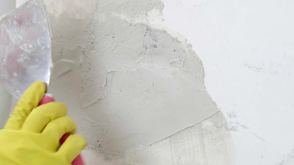 Plasterer Man Holding Putty Knife is Spackling Patching a Hole in White Wall