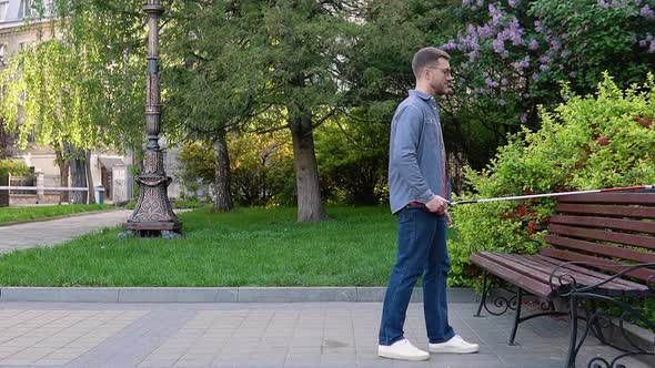 A Blind Man with a Cane Approaches the Bench and Sits Down