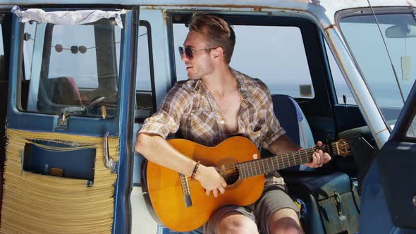 Guy sitting in van playing guitar on road trip