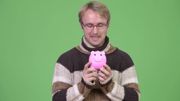 Studio Shot of Happy Handsome Man Thinking While Holding Piggy Bank