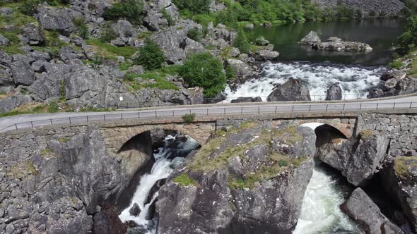 Road crossing old bridge built by rocks - River flowing from lake and below bridge - Mabodalen valle