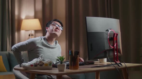 Asian Male Footwear Designer Having A Backache While Working On A Desktop Computer At Home