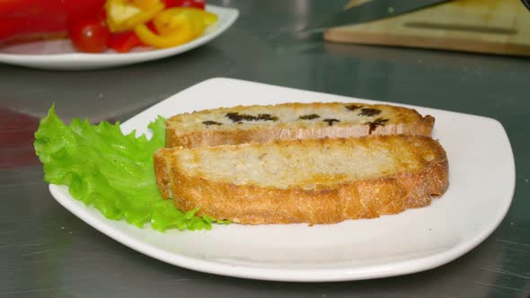 There is a Saucer with a Leaf of Green Lettuce and Two Toasted Slices of Bread on a Metal Tabletop