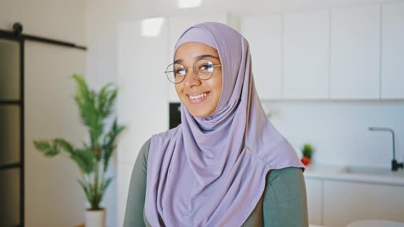 Smiling Muslim Woman in Glasses and Hijab Stands in the Kitchen