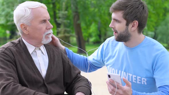 Funny Male Volunteer and Disabled Retiree Listening to Music in Headphones, Care