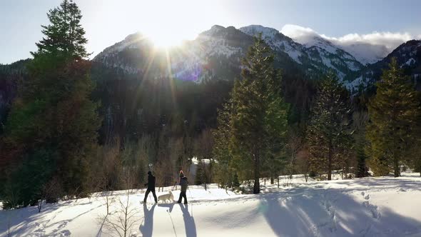 Couple snowshoeing with their dog as sun shines over mountain top