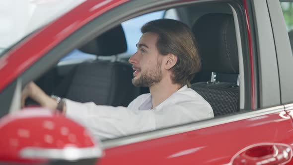 Excited Successful Young Man Cheering Purchase of New Automobile Sitting on Driver's Seat in
