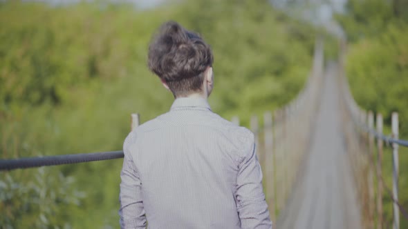 Guy Walks on Suspended Bridge in the Forest